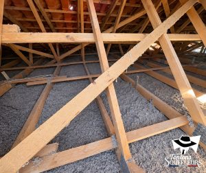 Vue d'ensemble de combles dont le sol est recouvert d'une couche régulière de ouate de cellulose grise, sous une charpente en bois et une toiture en tuiles